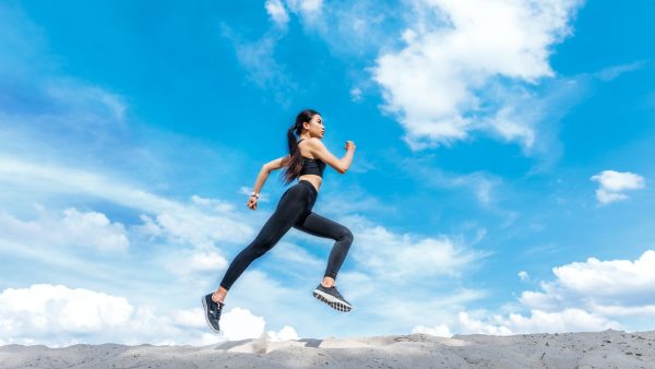 slim asian sportswoman running on sand against cloudy sky